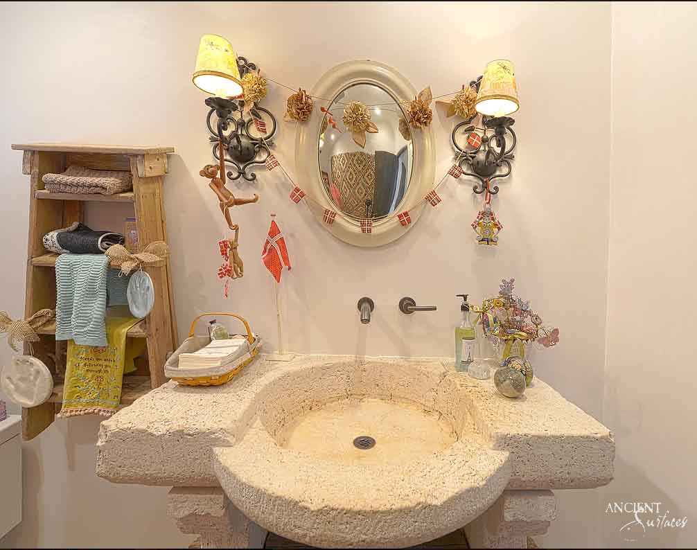 Reclaimed antique limestone vanity sink from Ancient Surfaces cut from one pale block, a wide slab top with a large shallow round basin and a rounded half apron curving forward beneath it