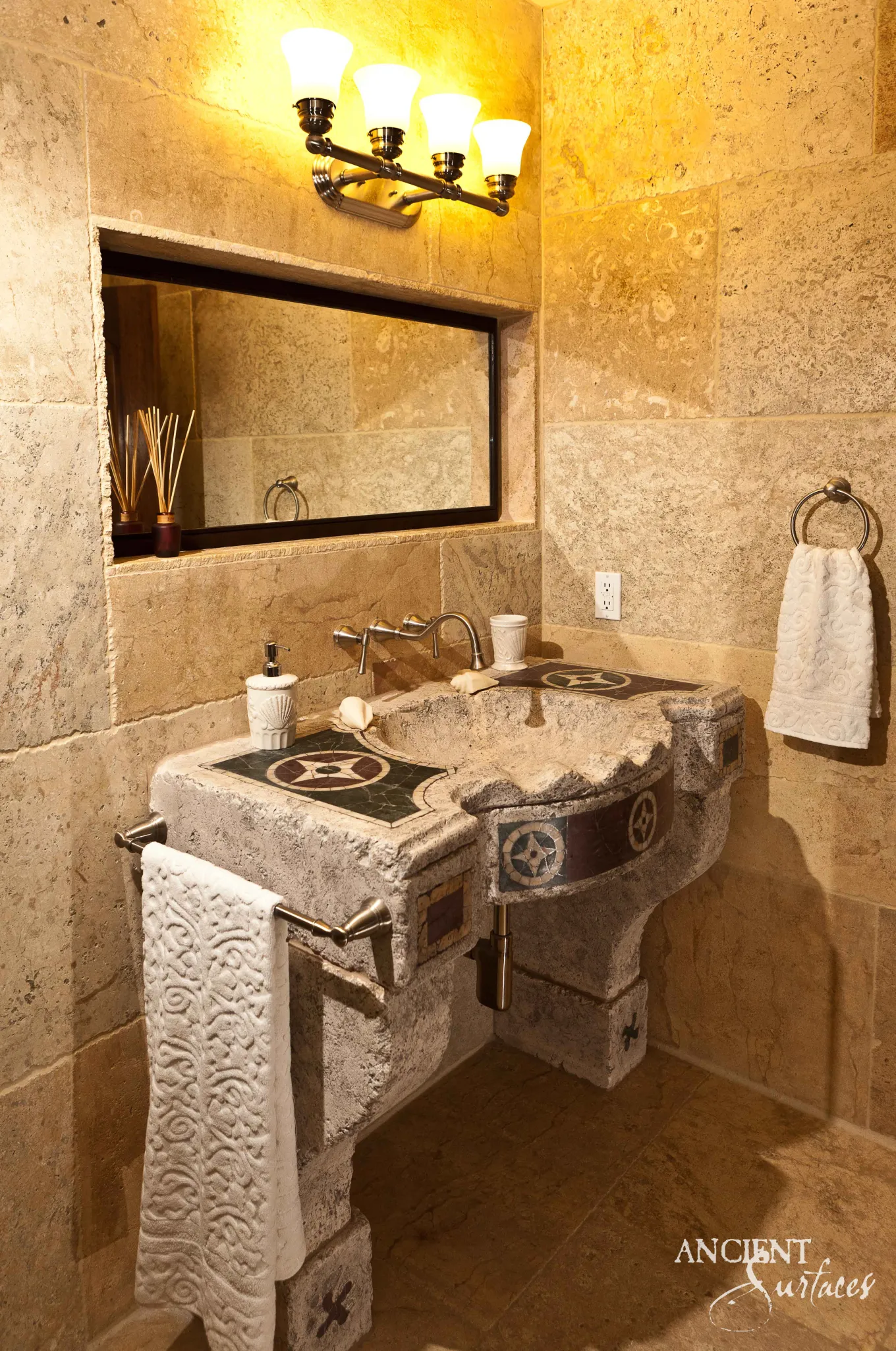Reclaimed antique limestone console sink from Ancient Surfaces in pitted silver grey stone, its deck and curved apron inlaid with dark panels holding pale rosettes, carried on two carved stone pier legs