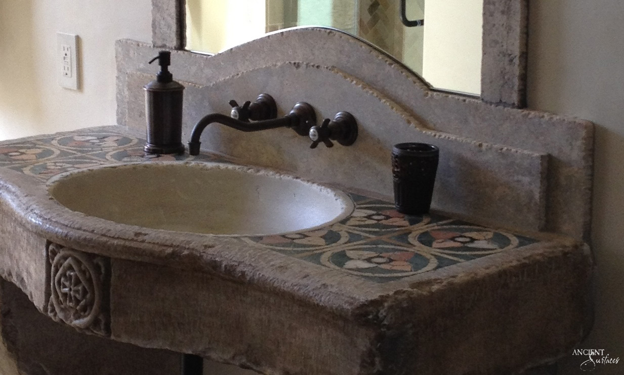 Reclaimed antique limestone vanity sink from Ancient Surfaces with a wide oval basin, an arched integral backsplash and patterned tile panels inlaid flat into the stone deck