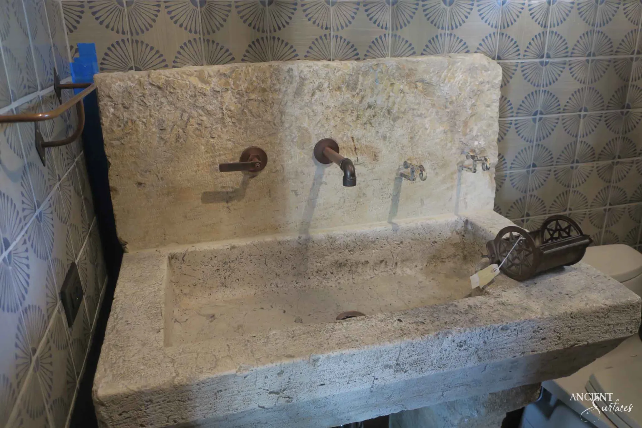 Long reclaimed antique limestone trough sink from Ancient Surfaces with a shallow basin, a flat drainage shelf and a tall limestone backsplash slab pierced for two bronze wall spouts