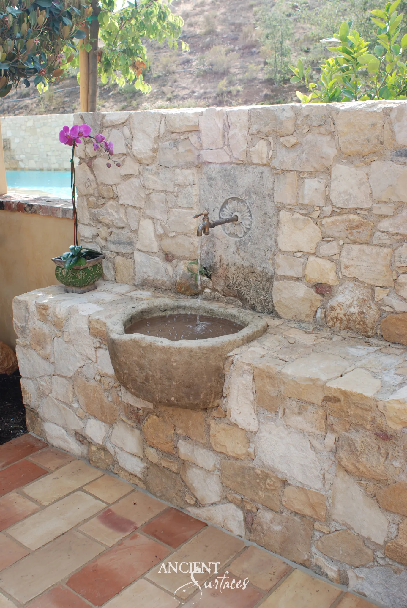 Wall mounted reclaimed antique limestone garden basin from Ancient Surfaces, half round with a heavy tapered underside and a rim worn soft by weather, built into a rubble stone wall