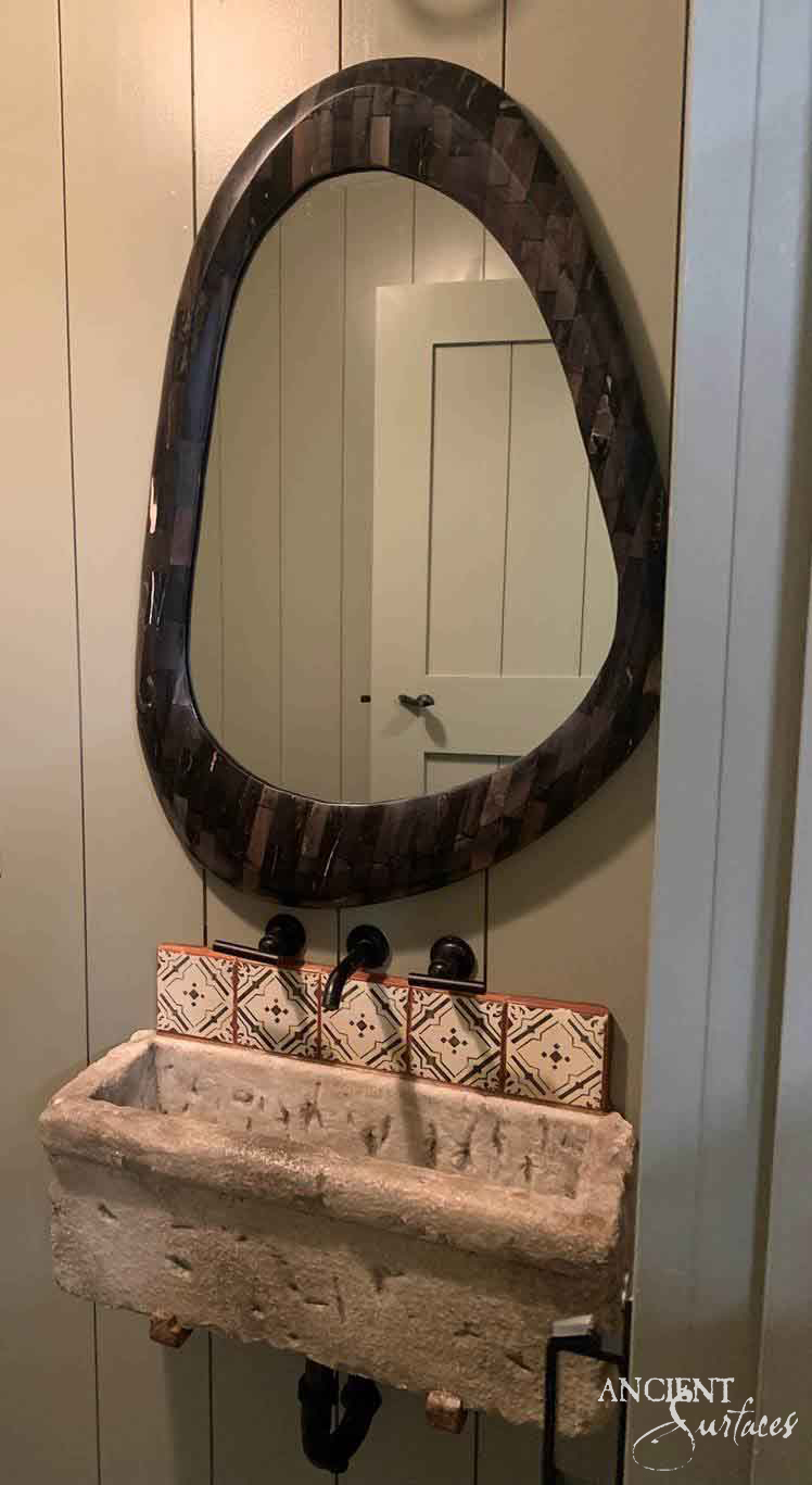 Small reclaimed antique limestone trough sink from Ancient Surfaces hung on the wall without a cabinet, its shallow flat floored basin behind an uneven worn rim and deeply chiselled outer faces