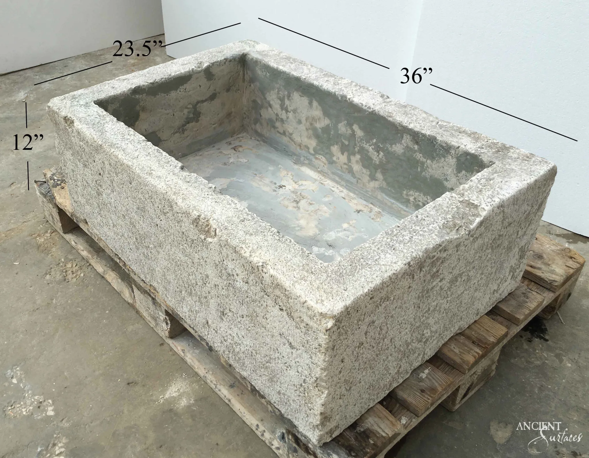 Rectangular reclaimed antique limestone trough sink from Ancient Surfaces on a timber pallet, thick square walls with a coarse weathered exterior and a grey stained basin, marked 36 by 23.5 by 12 inches